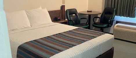 A hotel room with a large bed, a desk, two chairs, a lamp, and a picture on the wall.