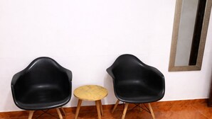 Two black chairs and a small round table in a room with wooden flooring and a mirror on the wall. - Three rooms AREAS by QuBeLab (Bello)