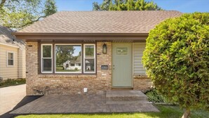 A single-story brick house with a front porch, a green door, and a small tree in the front yard. - Spacious 5-bedroom house in terrific Hopkins with open living and dining space. (Hopkins)