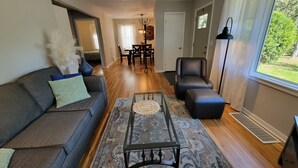 A modern living room with a sofa, ottoman, coffee table, and a dining area in the background. - Spacious 5-bedroom house in terrific Hopkins with open living and dining space. (Hopkins)
