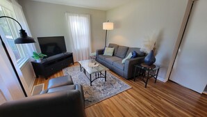 A living room with a sofa, TV, coffee table, and a lamp. - Spacious 5-bedroom house in terrific Hopkins with open living and dining space. (Hopkins)