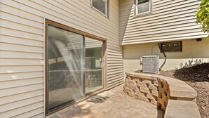 A house with a sliding glass door, a brick patio, and a stone retaining wall. - Spacious 5-bedroom house in terrific Hopkins with open living and dining space. (Hopkins)