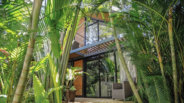 Een modern huis met grote glasramen, omringd door weelderig groen.