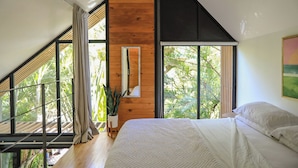 Een slaapkamer met een groot bed, houten wanden en grote ramen met uitzicht op groen.