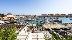 A marina with numerous boats docked, a building with a green roof, and a clear blue sky.