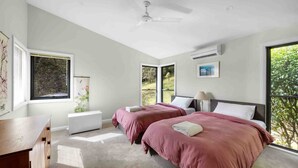 A bedroom with two beds, a ceiling fan, an air conditioning unit, and large windows offering a view of greenery. - Wombat Wallows - Kangaroo Valley (Kangaroo Valley)
