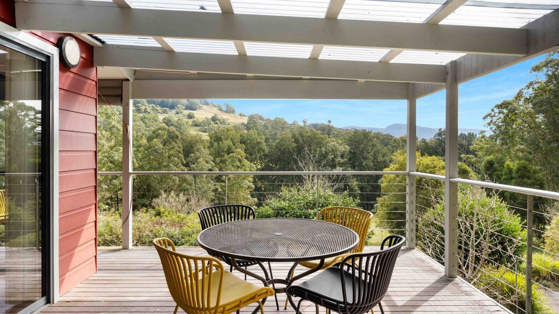 A covered outdoor area with a round table and chairs, overlooking a forested landscape.