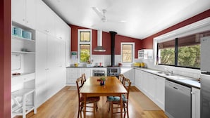 A modern kitchen with white cabinets, a wooden dining table, and a black stove. - Wombat Wallows - Kangaroo Valley (Kangaroo Valley)