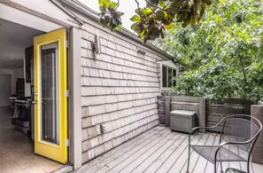A covered patio with a wooden deck, a yellow door, and a metal chair.