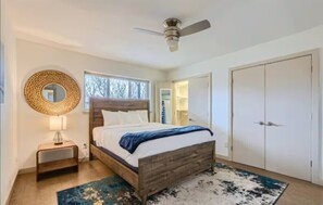 A bedroom with a wooden bed, a round mirror, a ceiling fan, and a wardrobe.