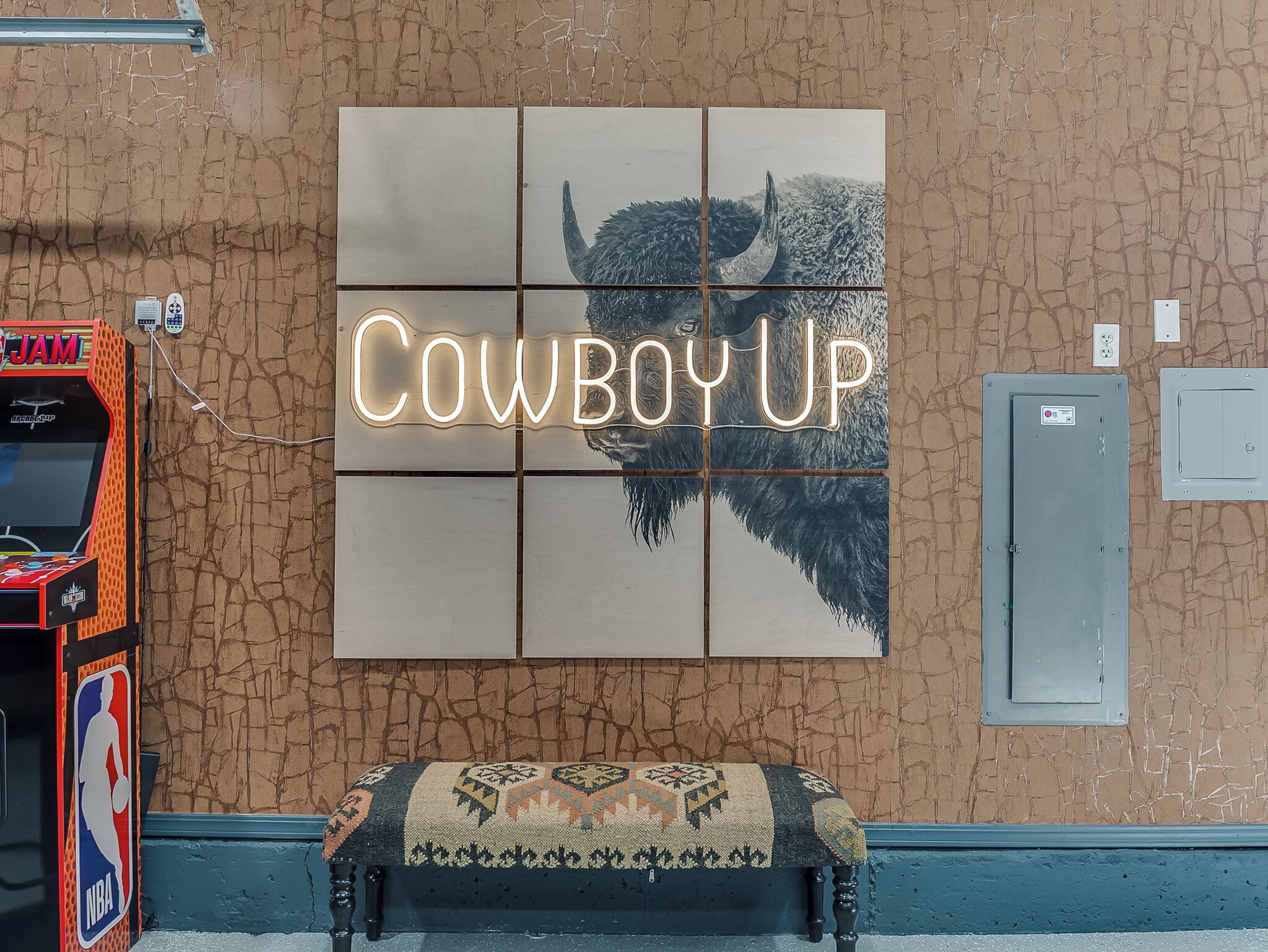 Un mur orné d’un panneau néon avec l’inscription « Cowboy Up » et d’une silhouette de bison.