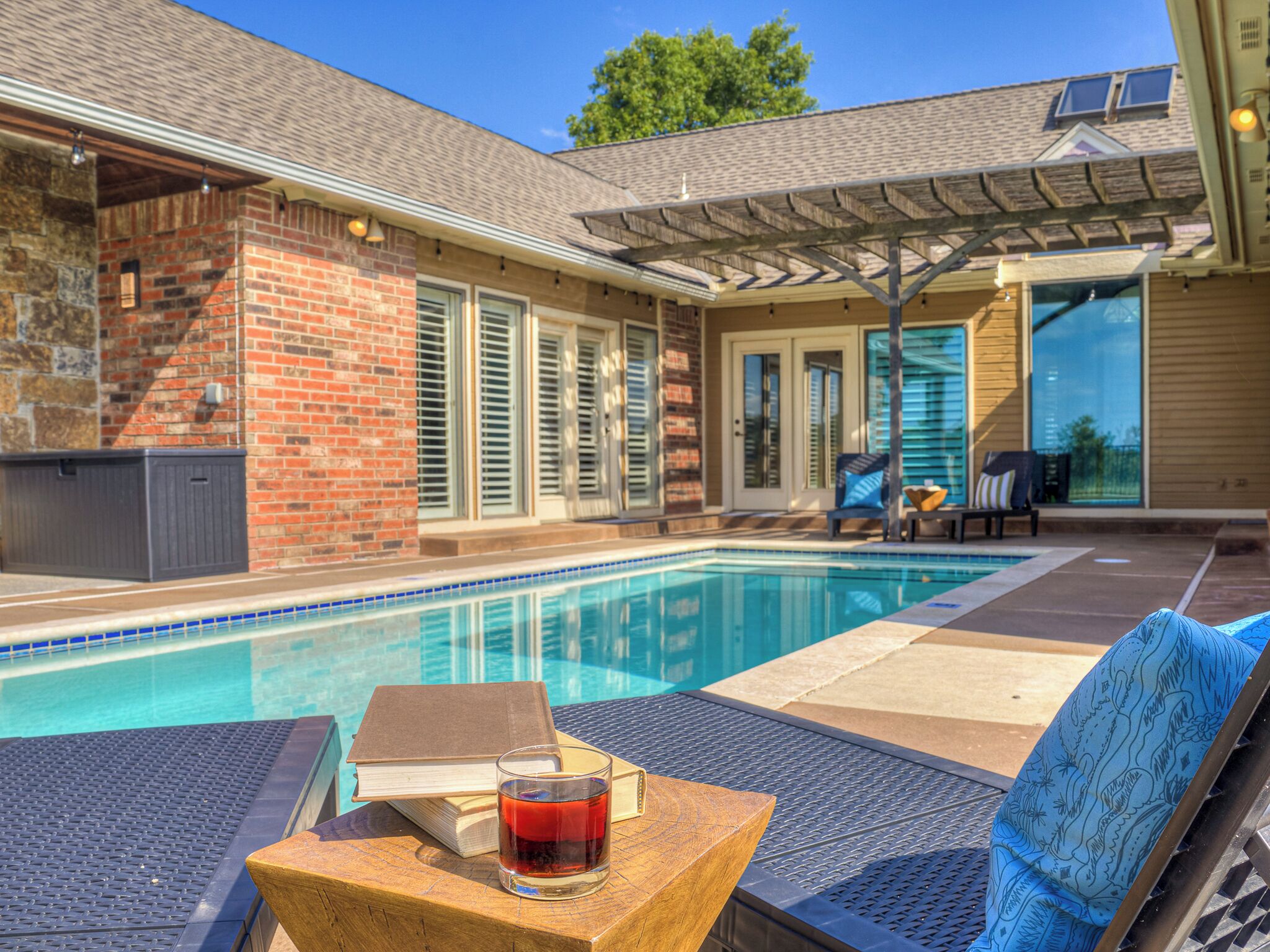 A poolside area with a brick wall, a covered patio, and outdoor furniture.
