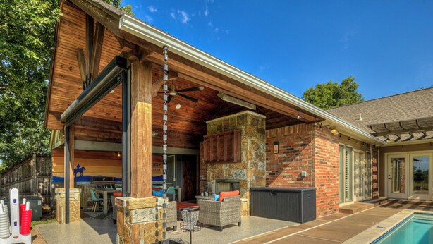 Un patio extérieur couvert avec une piscine, des piliers en pierre et un espace barbecue.