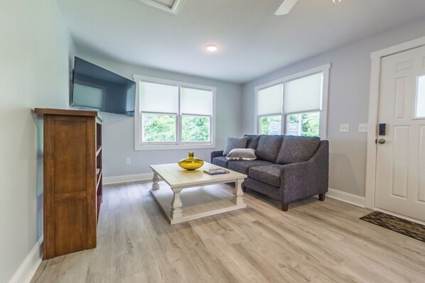 Un salon avec un parquet de couleur claire, un canapé gris, une table basse blanche sur laquelle se trouve un bol jaune, et un meuble en bois.