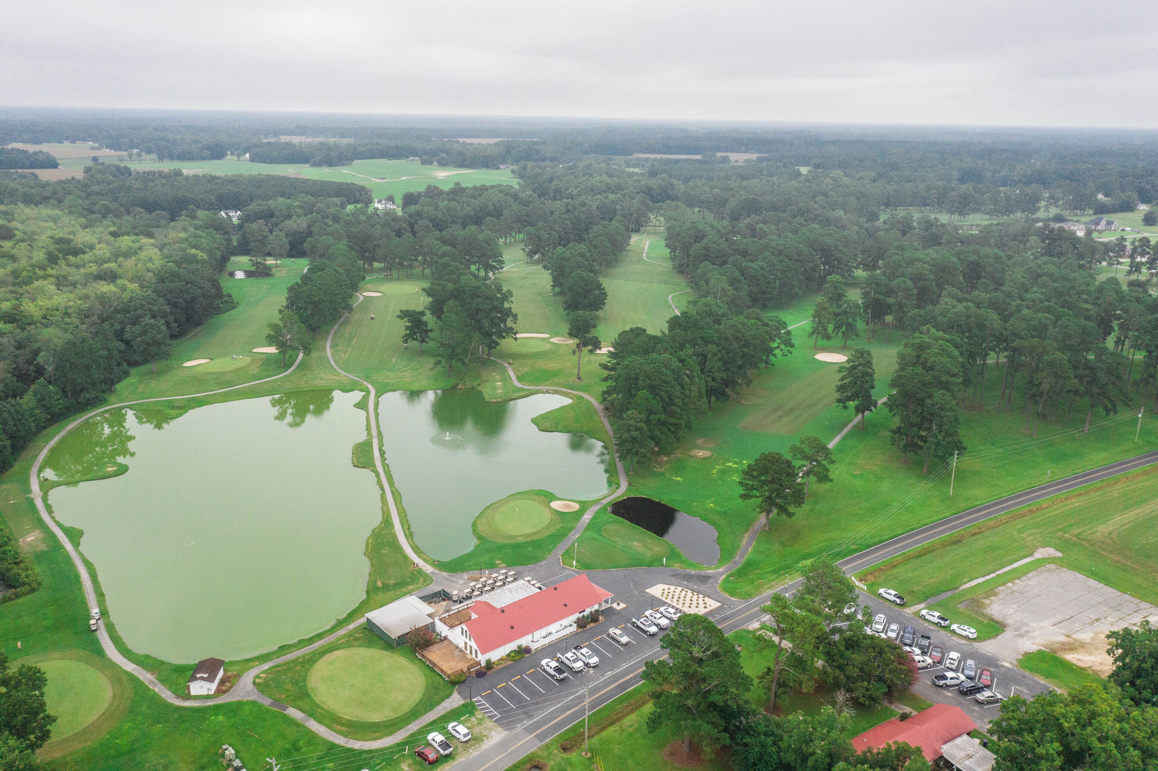 Vista aèria d'un camp de golf amb diverses basses, un aparcament i un edifici amb teulada vermella.