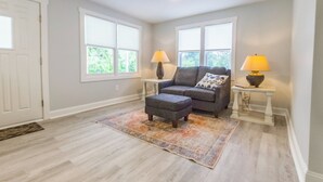 Un salon avec un canapé gris, un pouf, deux lampes sur des tables d’appoint et un tapis à motifs.