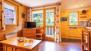 A wooden cabin interior with a dining area, kitchen, and a TV. - Cimes 2 #21 - 6 guests - Ski in - Ski out (Les Allues)