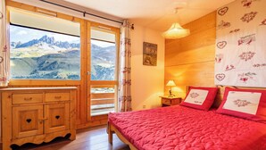 A bedroom with a wooden bed, a view of mountains through a large window, a wooden dresser, and a painting on the wall. - Cimes 2 #21 - 6 guests - Ski in - Ski out (Les Allues)