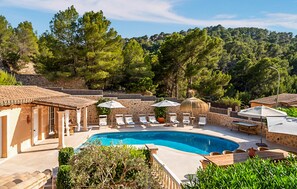 A pool area with lounge chairs and umbrellas, surrounded by stone walls and trees. - Stunning home in Puerto de Andratx (Puerto de Andratx)