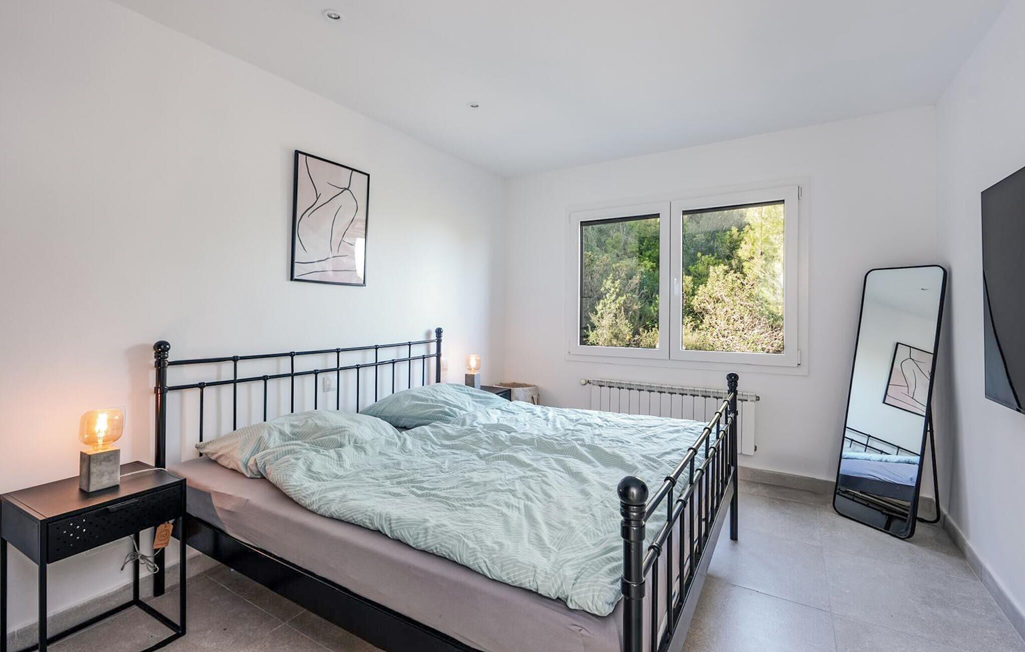 A bedroom with a bed, bedside tables, a window, and a mirror.