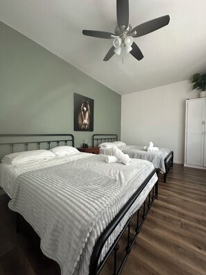 A hotel room with two beds, a ceiling fan, a painting on the wall, and a wardrobe.