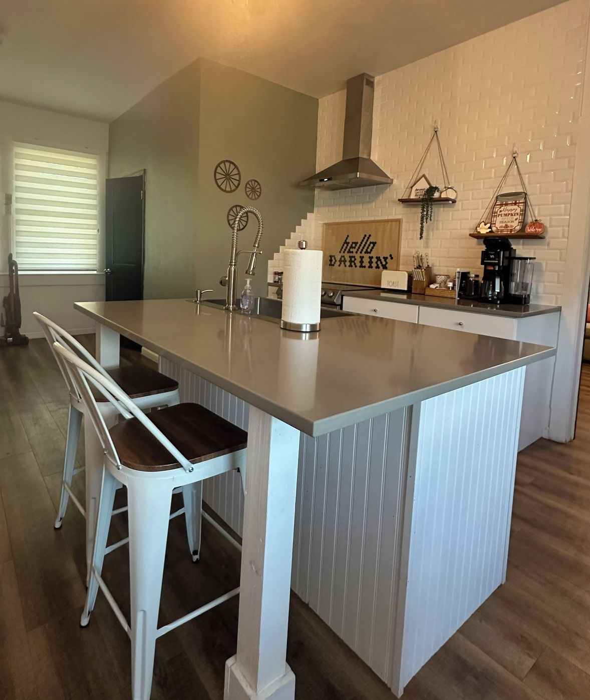A kitchen with a central island, white bar stools, a coffee machine, and a sign that reads 'hello DARLIN''.