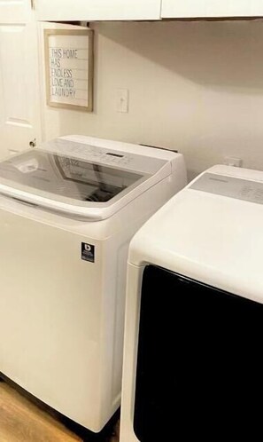 A laundry room with two white washing machines and a sign above them that reads "THIS HOME HAS ENDLESS LOVE AND LAVENDER".