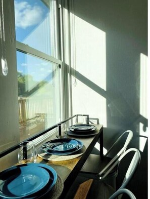 Un coin repas avec une table dressée pour deux personnes, une fenêtre donnant sur l’extérieur et une chaise avec un cadre en métal.