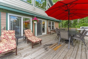 A wooden deck with outdoor furniture, a dining table, and a red umbrella.