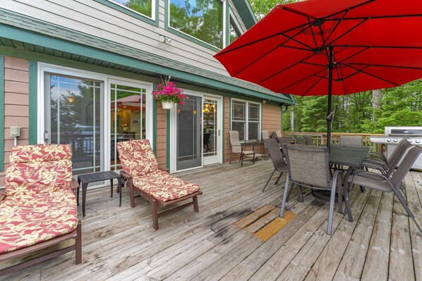 A wooden deck with outdoor furniture, a dining table, and a red umbrella.