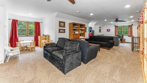 A living room with a sofa, a dining table with chairs, a ceiling fan, and a television.