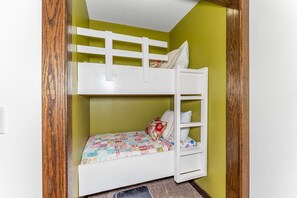 Una cama litera con colcha acolchada, un almohadón y una escalera.
