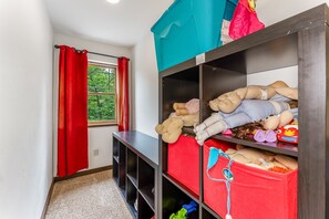 A room with a window, red curtains, a bookshelf, and a storage unit with various items.