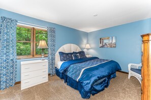 A bedroom with a bed, a dresser, a chair, a window with curtains, and a painting on the wall.