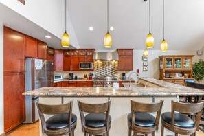 A kitchen with wooden cabinets, granite countertops, stainless steel appliances, and pendant lighting.