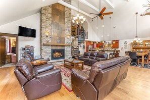 A spacious living room with leather sofas, a fireplace, a stone accent wall, and a dining area with wooden furniture.
