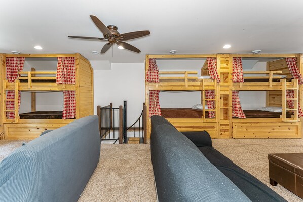 A room with bunk beds, a ceiling fan, and a sofa.
