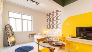 A modern room with a bed, a dining area with yellow chairs, a TV, and a large window. - Cozy 6 Minutes From Copacabana Beach Br710 (Rio de Janeiro)