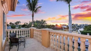 Un balcon offrant une vue sur un coucher de soleil, des palmiers et le paysage urbain.