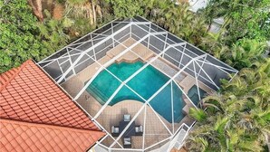 Vue aérienne d’un espace piscine doté d’un couvercle géométrique, entouré d’une végétation luxuriante et d’une structure au toit rouge.