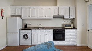 A compact kitchen with white cabinetry, a washing machine, a refrigerator, a microwave, and a stove. - Golden Star AV – Modern Retreat in Funchal (Funchal)