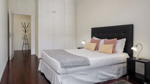 A bedroom with a large bed, white walls, a black headboard, and a nightstand with a lamp. - Golden Star AV – Modern Retreat in Funchal (Funchal)