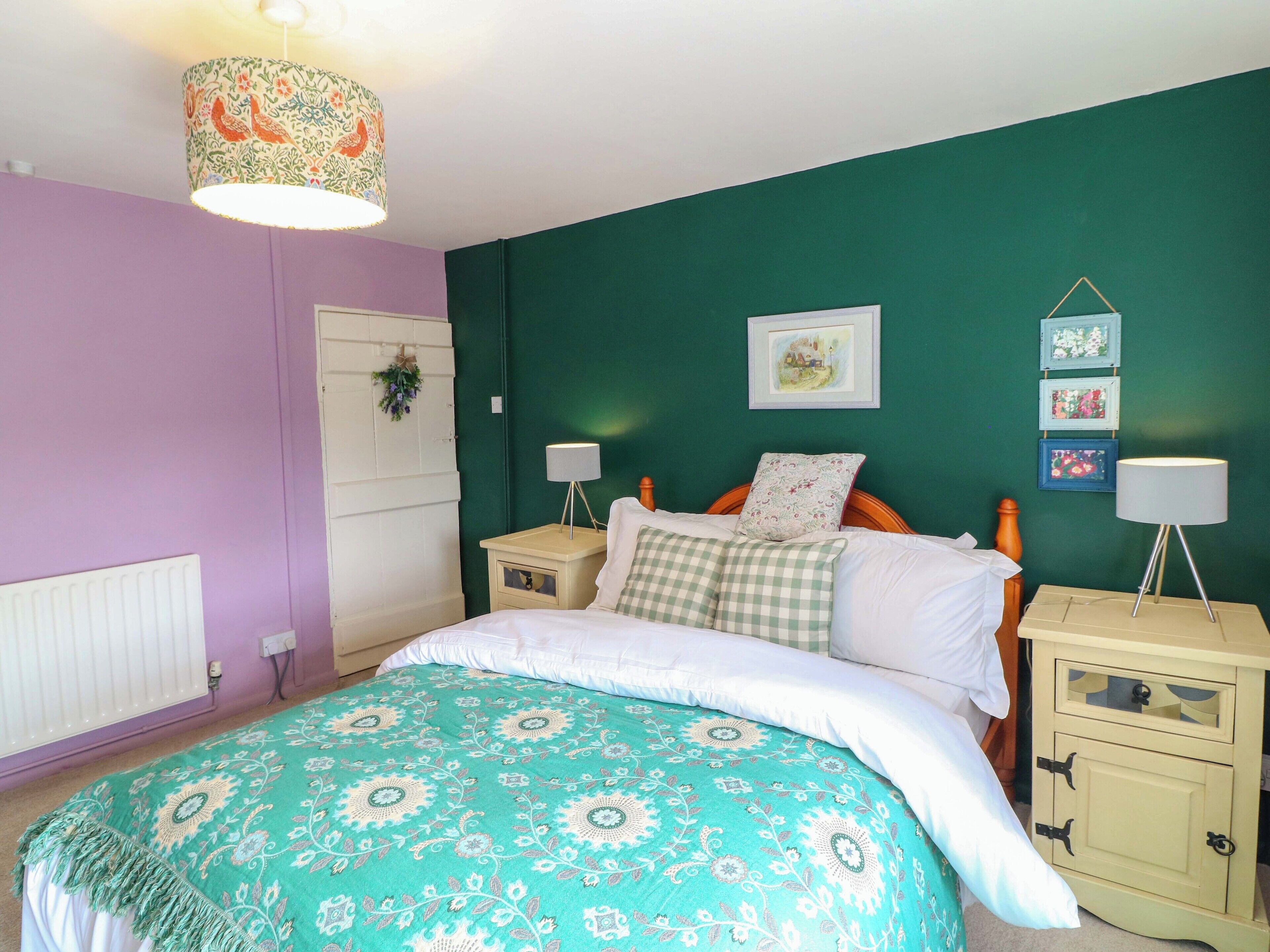 Een slaapkamer met een bed, twee nachtkastjes, een dressoir, een hanglamp en een aan de muur bevestigd schilderij.