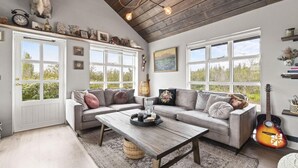 A cozy living room with a wooden ceiling, a grey sofa with multiple cushions, a coffee table, and a guitar. - Beautiful cottage in a great location. Golden circle (Bláskógabyggð)