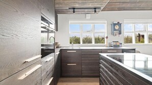 Une cuisine moderne avec des meubles de couleur sombre, un grand îlot central et une fenêtre donnant sur un espace verdoyant.