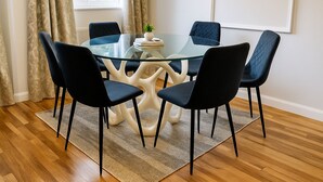 Una mesa de vidrio redonda rodeada por seis sillas negras con base blanca, sobre un piso de madera con alfombra color beige.