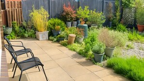 Un patio con mobiliario exterior, diversos maceteros y una valla de madera.