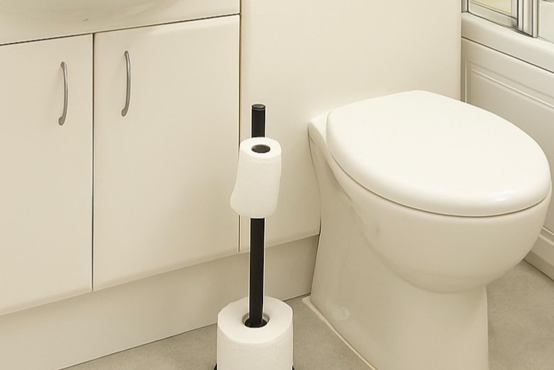 A toilet paper holder with a roll of toilet paper in a bathroom with a white toilet and a cabinet with two handles.