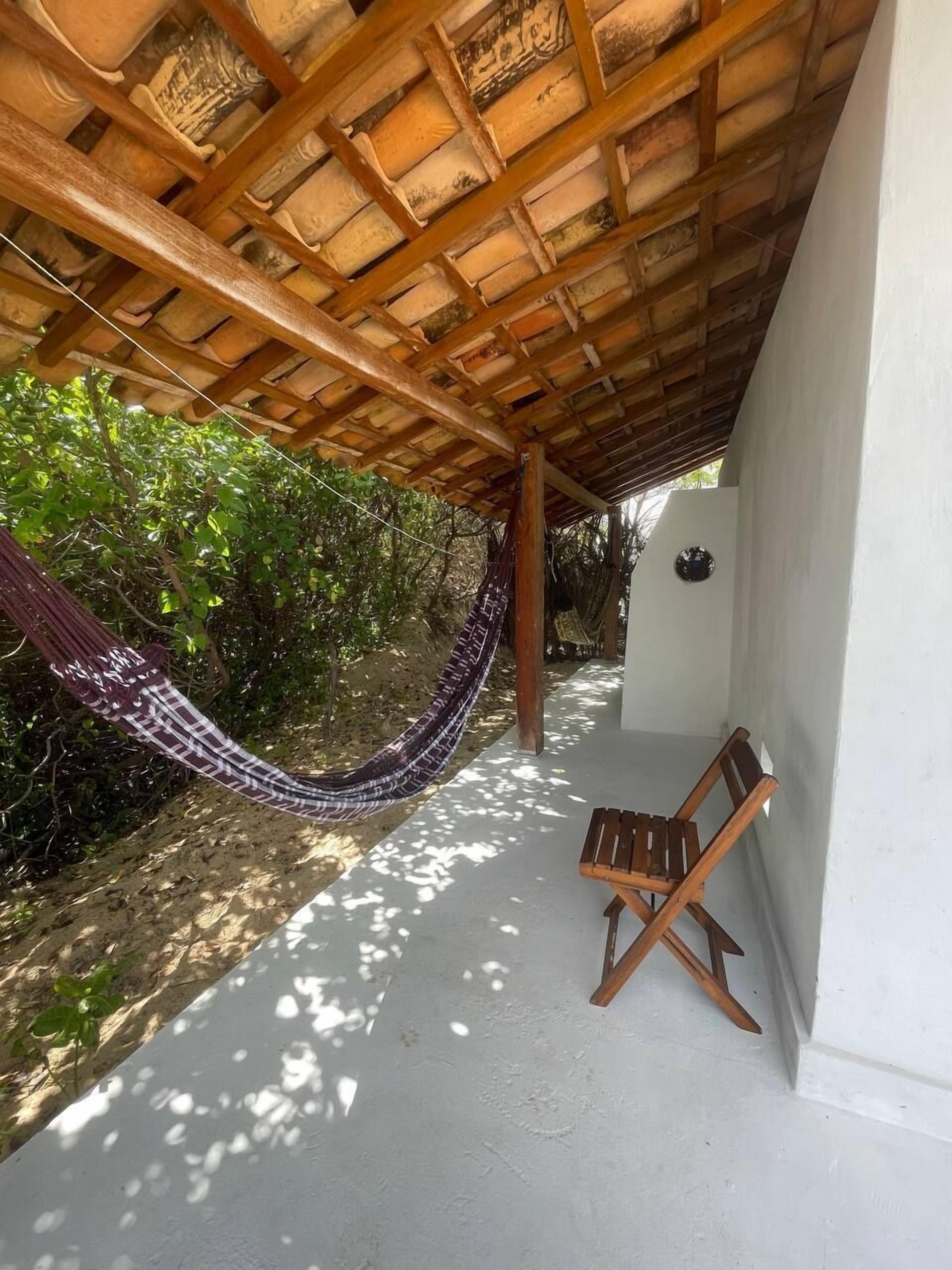 Een hangmat onder een houten pergola, een houten stoel en een witte muur.