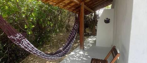 Een hangmat onder een houten pergola, een houten stoel en een witte muur.